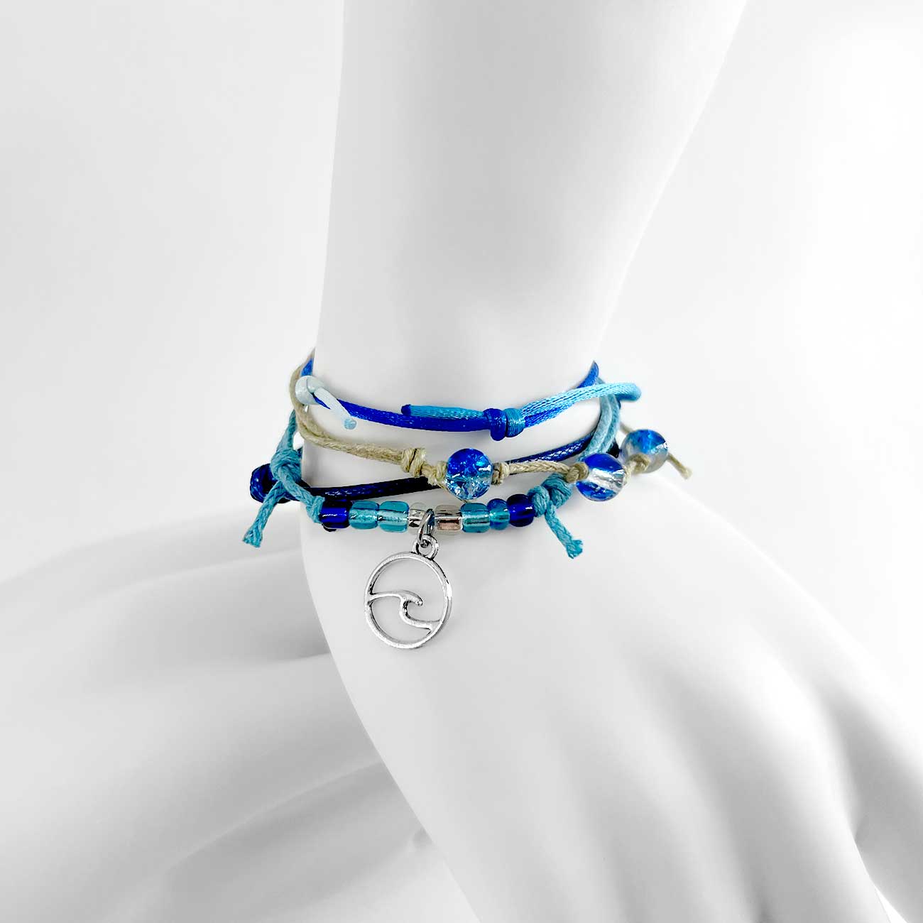 wave bracelet pack stacked on a white mannequin ankle with blue glass beads, adjustable cords and silver-tone wave charm.