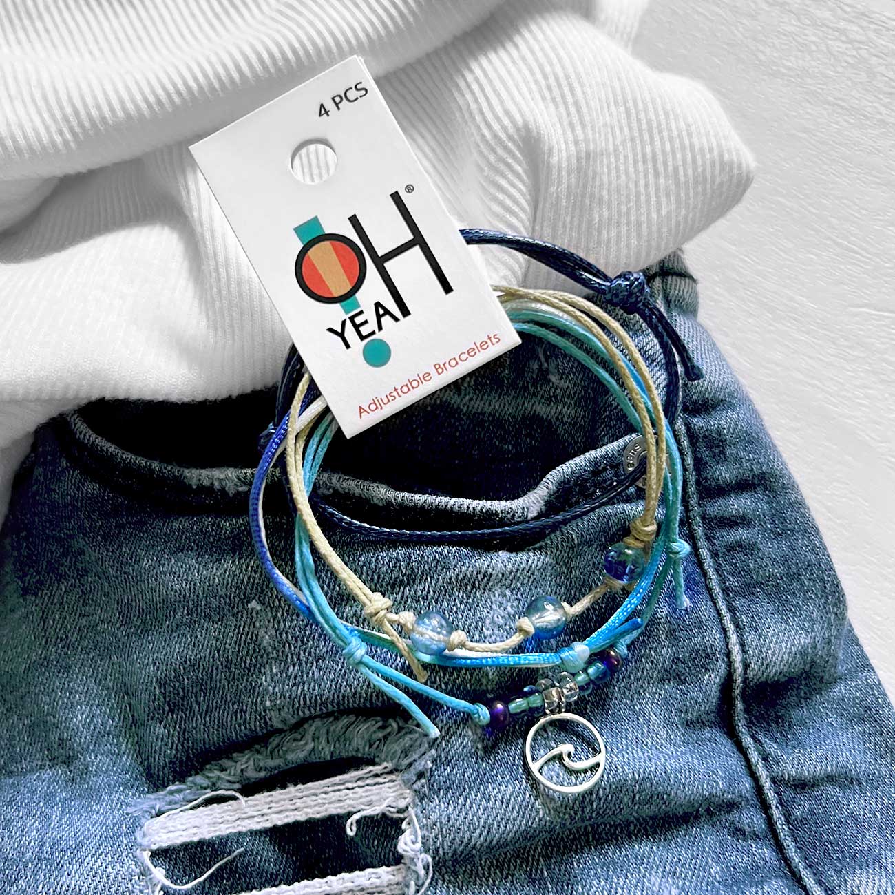 wave bracelet pack with blue glass beads and silver-tone wave charm on ripped denim beneath white fabric with O Yeah tag.
