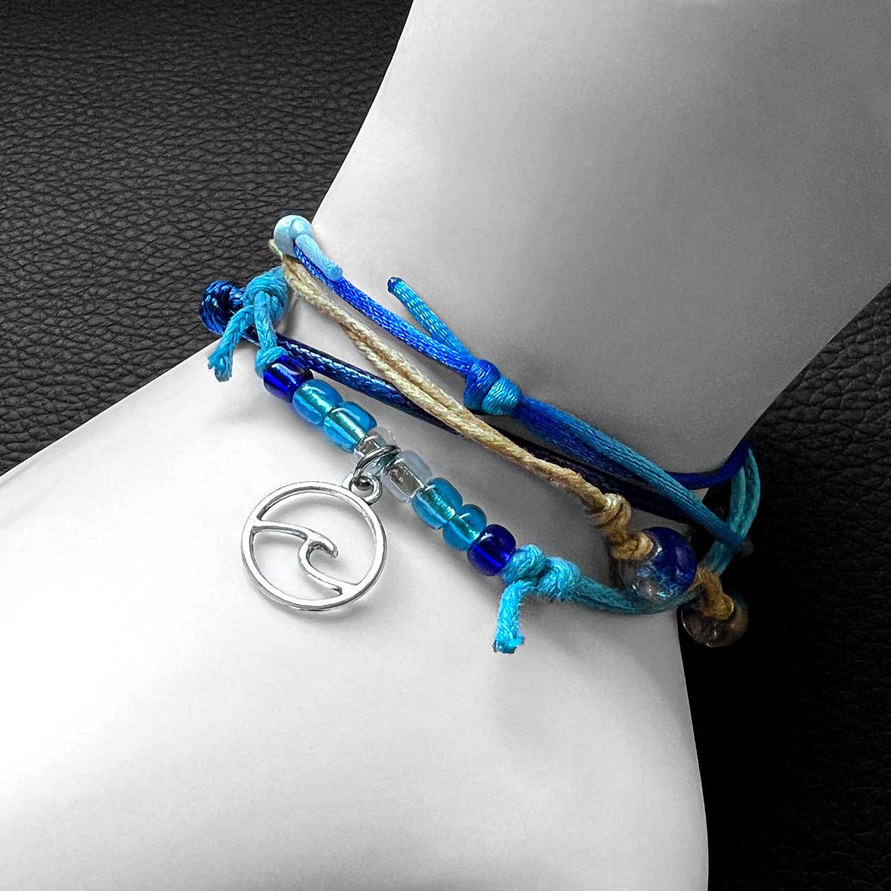 wave bracelet pack on white mannequin wrist with blue glass beads and silver-tone wave charm against black background.