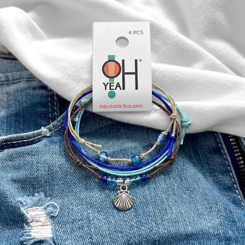 seashell bracelet set with blue cords, glass beads and silver-tone shell charm on denim beside a white shirt and O Yeah tag.