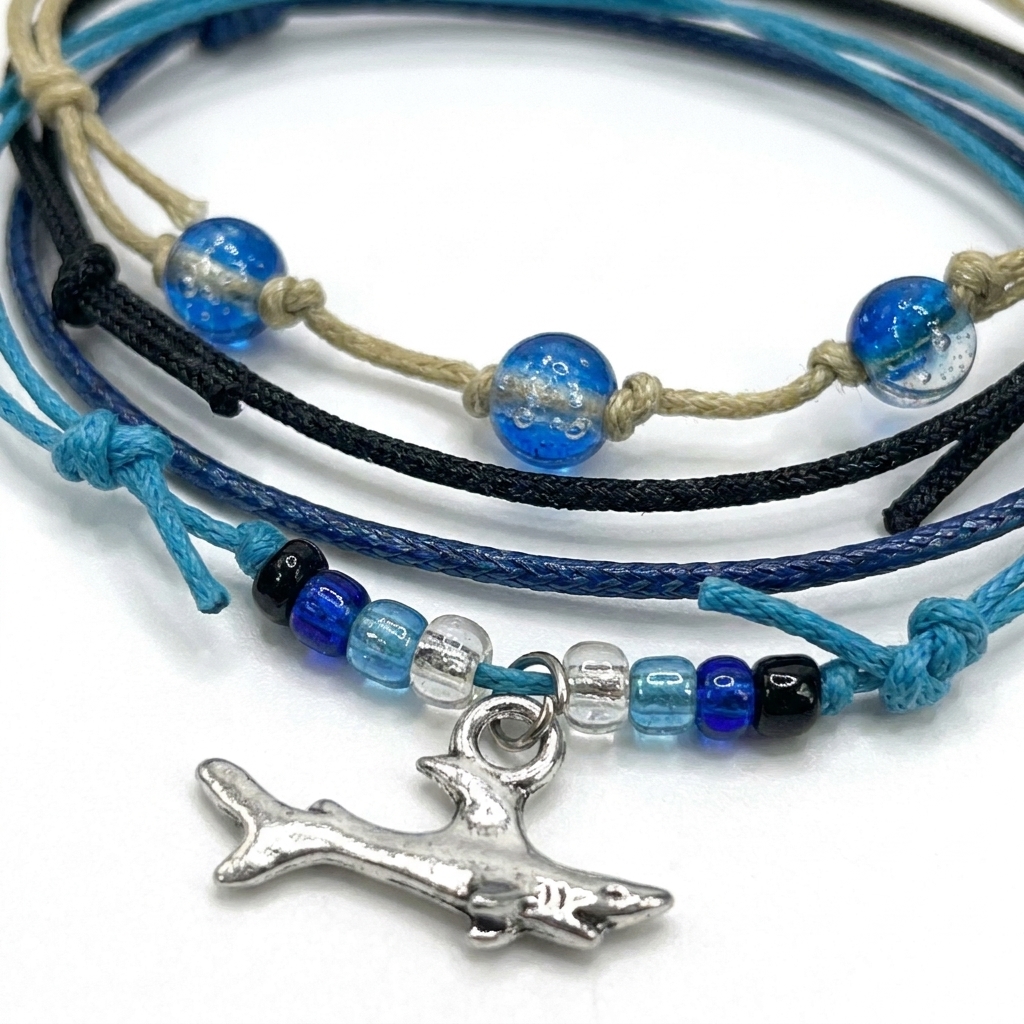 shark bracelet set close-up showing silver-tone shark charm, blue glass beads and layered blue, black and beige cords.