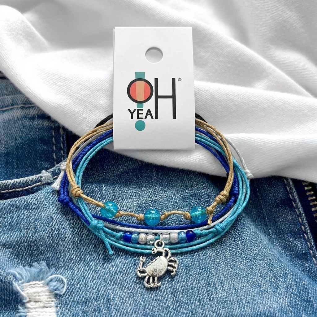 crab bracelet stack with blue beads, silver-tone crab charm and O Yeah tag displayed on denim beneath a white shirt.