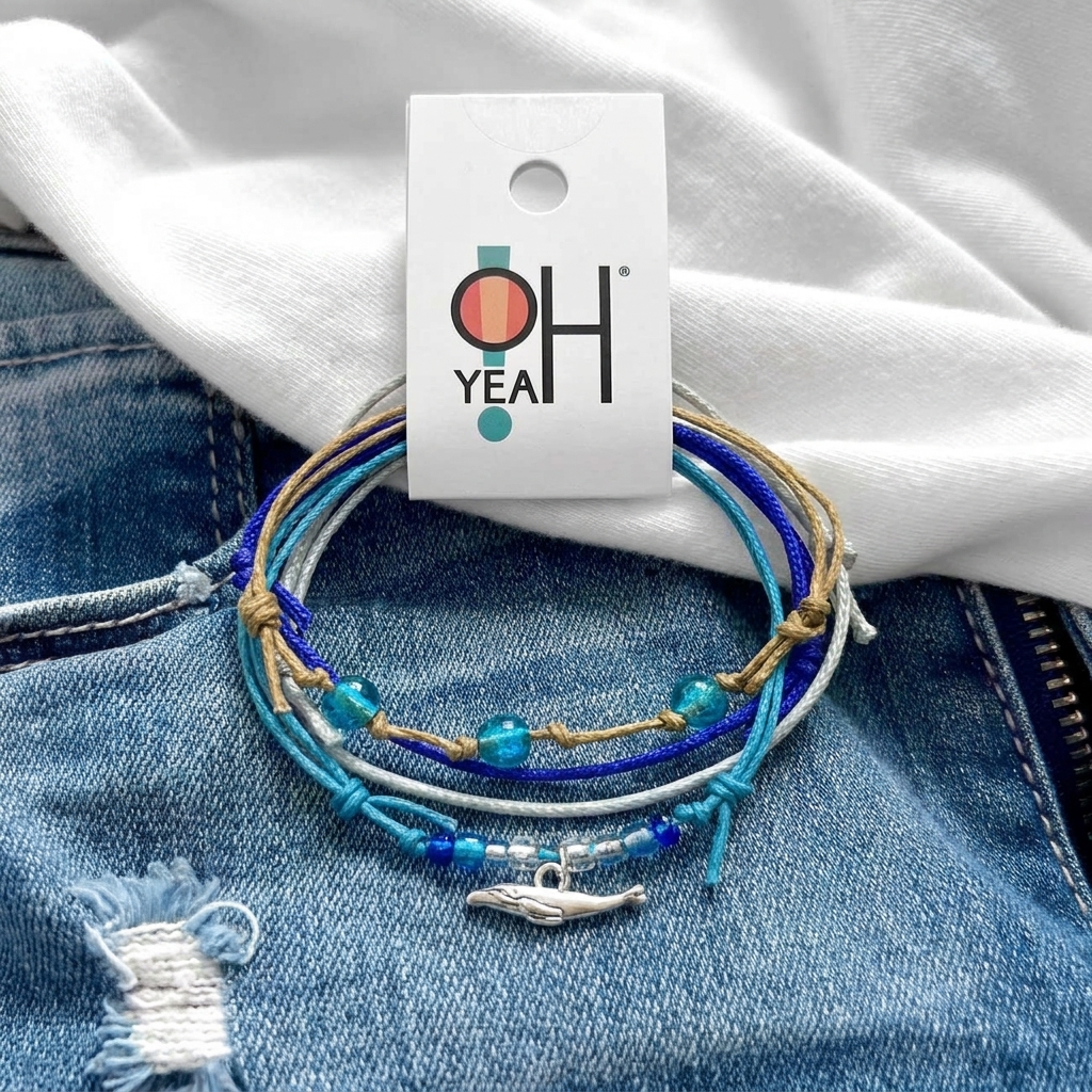whale bracelet set with blue beads and silver whale charm on faded jeans beneath a white shirt and O Yeah tag.