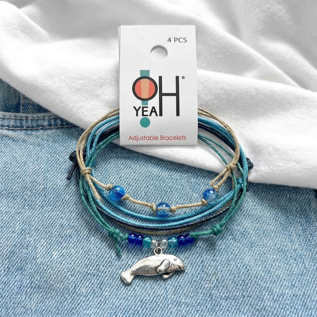 manatee bracelet stack with blue and turquoise cords, silver-tone charm and O Yeah hang tag on denim with white fabric.