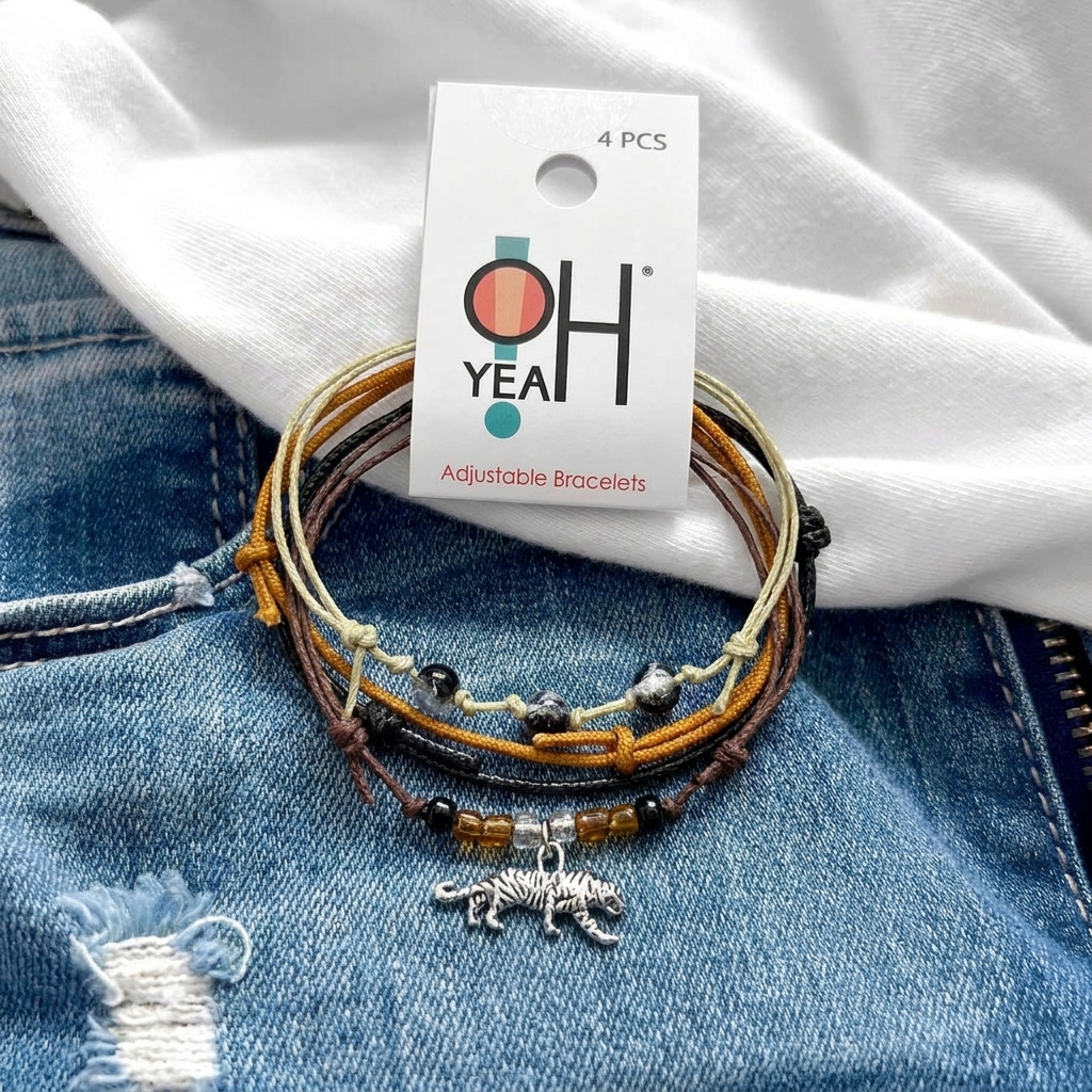 tiger bracelet stack with orange, brown and beige cords, glass beads and silver-tone tiger charm on denim with O Yeah tag.